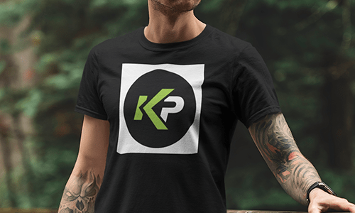 A person wearing a black t-shirt with a KP logo in green and white inside a black circle, centered on the shirt, stands outdoors against a blurred background of green trees—perfect for anyone who loves discussing File Types.