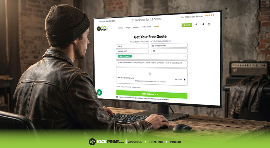 A person in a leather jacket sits at a rustic desk using a desktop computer, viewing KickPrint.com's website form to get Instant Screen Print Pricing and a free quote for apparel, printing, and promo services.