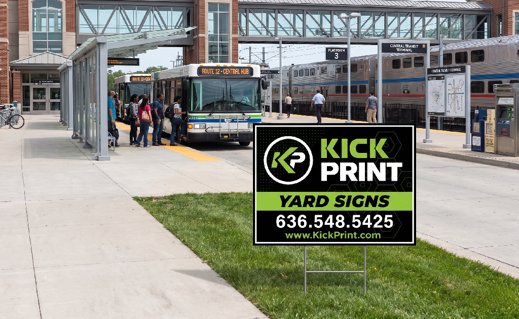 People board a city bus at a transit station with trains in the background. In the foreground, a Kick Print Yard Signs display advertises printing services with a phone number and website.