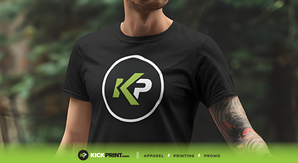 A person wearing a black t-shirt with a circular KP logo in green and white, subtly greeting with "Hello world." The image footer displays KICKPRINT.com and the words Apparel, Printing, and Promo on a green bar.