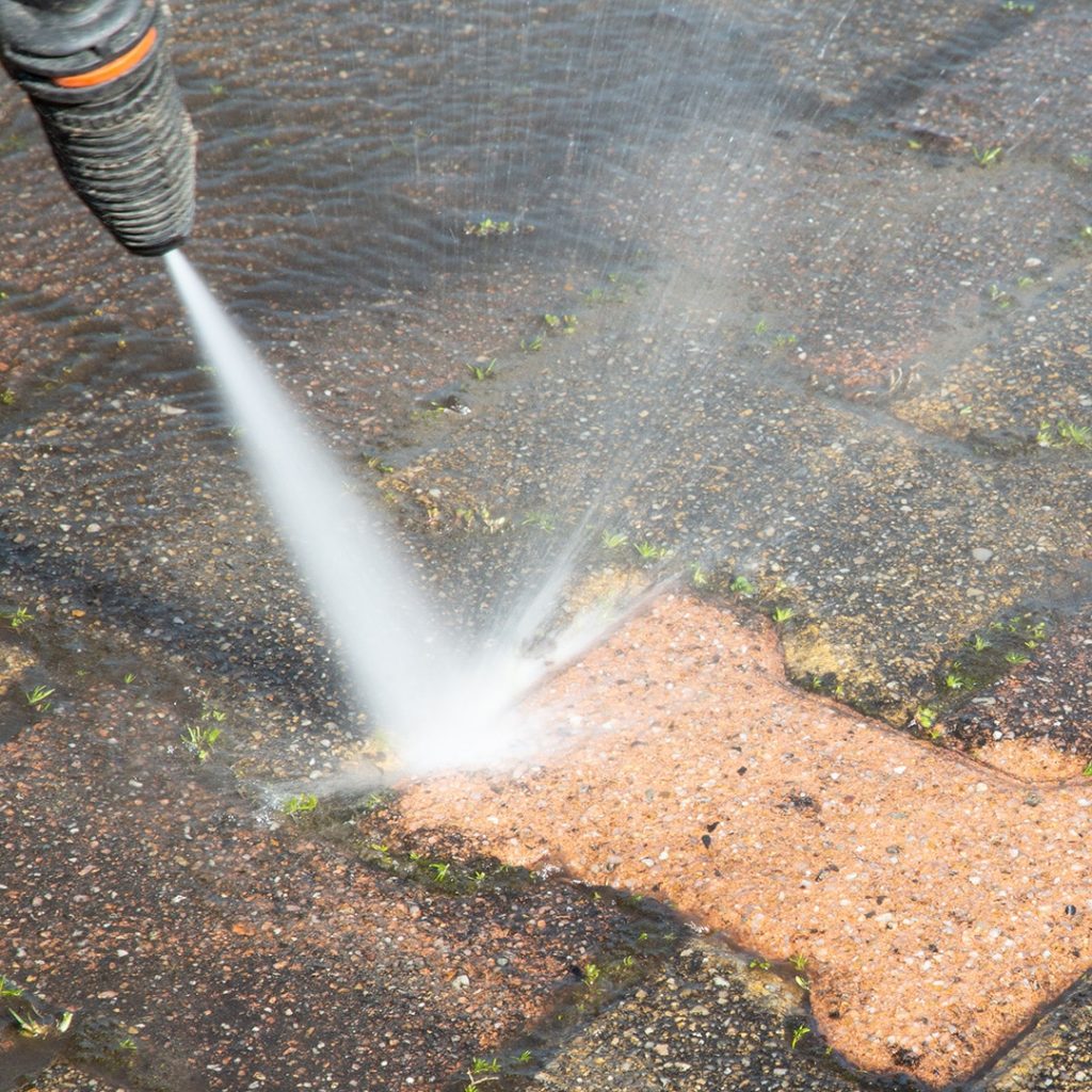 A pressure washer sprays water onto a stone pavement, cleansing dirt and revealing a cleaner, lighter section while shielding your shirts: safeguarding and cleansing amid pressure washing the darker, unwashed areas.