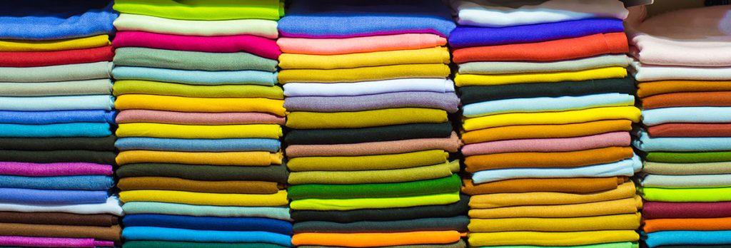 Stacks of neatly folded fabric in a wide variety of vibrant colors, arranged in thoughtful rows and columns—perfect for anyone comparing the Battle of the Cotton Titans: Bella Canvas vs. Next Level—who will be your supreme T-shirt brand?.