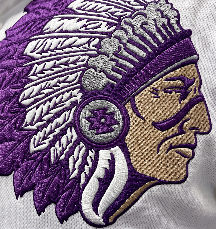 Embroidered patch featuring a person in a feathered headdress, crafted with purple, white, and gray thread on white fabric. The design showcases intricate embroidery details and reflects the artistry found in Jackson Mississippi.