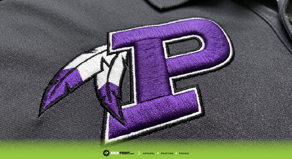 Close-up of an embroidered purple letter P with two white and purple feathers on dark gray fabric. A green strip with KICK-PRINT branding, embroidery and screen printing service icons appears at the edge. Kansas City craftsmanship shines through.