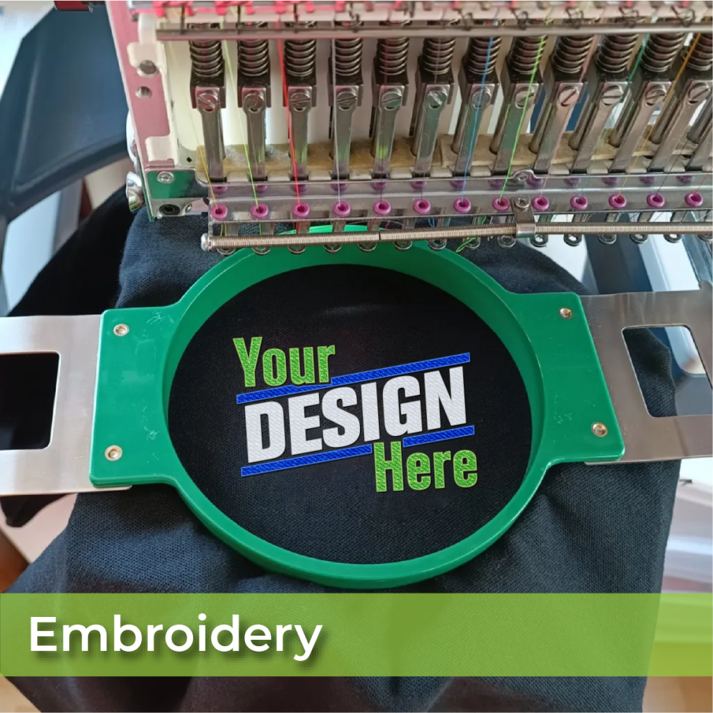 An embroidery machine stitches black fabric in a green hoop, showing Your DESIGN Here in green, blue, and white. The word Embroidery appears in a green banner below. Kick Print: Kirkwoods Premier Destination for Screen Printing Excellence!.