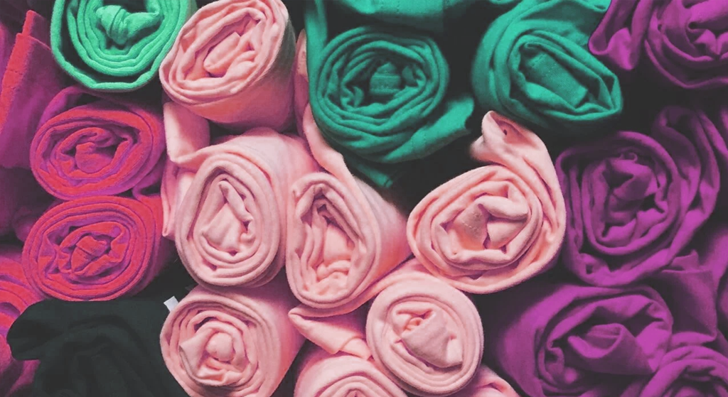 Rolls of colorful fabric arranged closely together, featuring shades of pink, green, and purple—perfect for crafting a vibrant charity t-shirt design with a textured and eye-catching pattern.