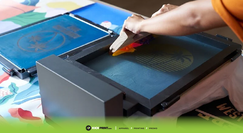 A person uses a squeegee to apply ink through a screen printing frame, creating a design on fabric. The setup includes professional screen printing screens and colorful ink, with a floral-patterned surface underneath.