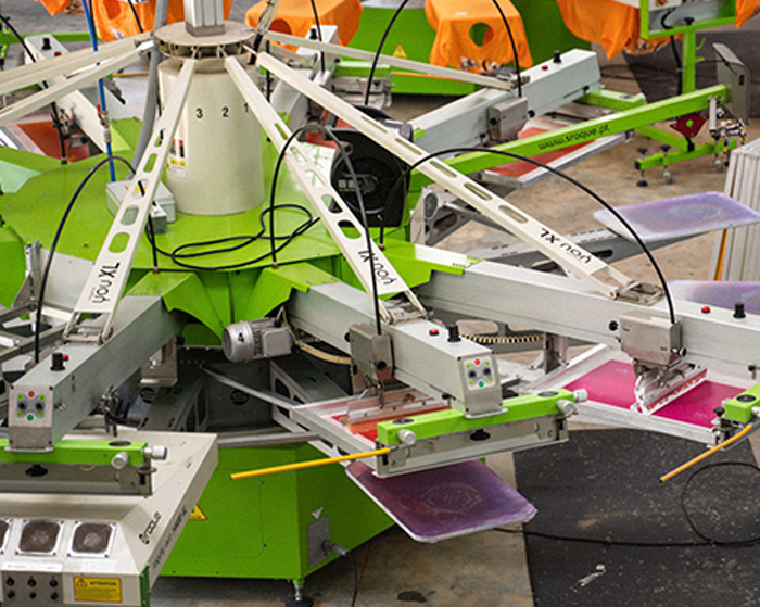 A close-up view of an automated screen printing machine with multiple arms, often found in Missouri screen printing companies, each holding screens and squeegees, used for printing designs on garments in a factory setting.