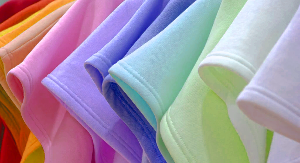 A close-up view of neatly hung T-shirts in a row, displaying a gradient of pastel colors—including pink, purple, blue, green, and white—showcasing quality prints from professional screen printing services.