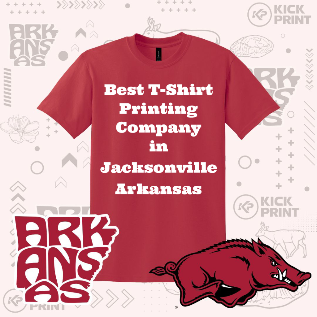 A red t-shirt with the text “Best T-Shirt Printing Company in Jacksonville Arkansas” in bold white letters. The background features “ARKANSAS” graphics, a wild hog illustration, and the Kick Print logo.