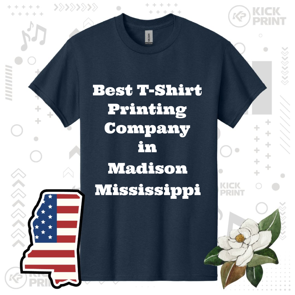 A navy blue t-shirt with the text Best T-Shirt Printing Company in Madison Mississippi in bold white letters, shown on a background with a USA-shaped flag, a magnolia flower, and graphic elements.