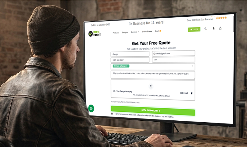 A man in a dark jacket and beanie is sitting at a desk, using a desktop computer to fill out an online form for a free quote on the Fast T-Shirt Printing Company website. The screen displays fields for personal and project details.